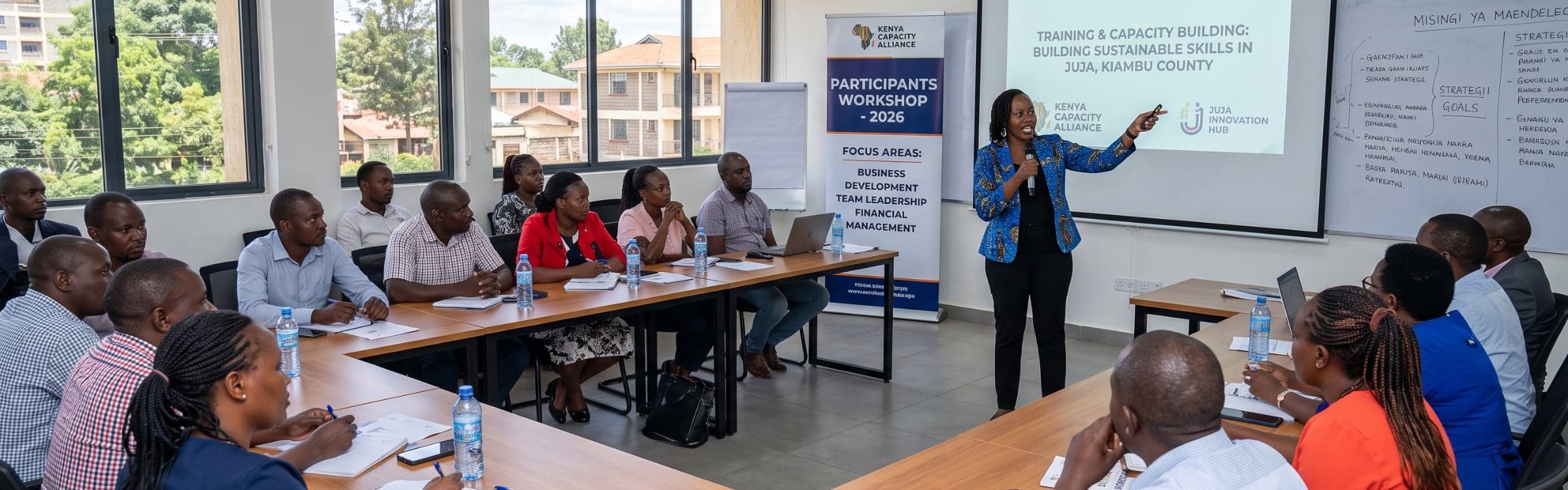 A trainer presenting to participants seated around tables in a workshop room.