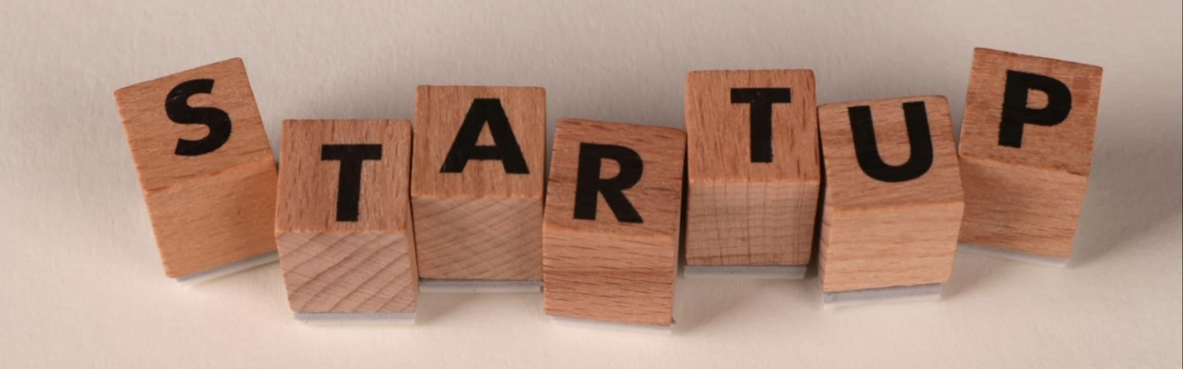 Seven wooden letter blocks arranged in a shallow arc on a pale surface, spelling the word STARTUP.